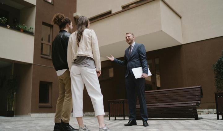 A realtor converses with a couple in a modern apartment courtyard.