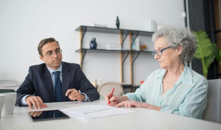 Elderly woman signing paperwork in modern office with consultant.